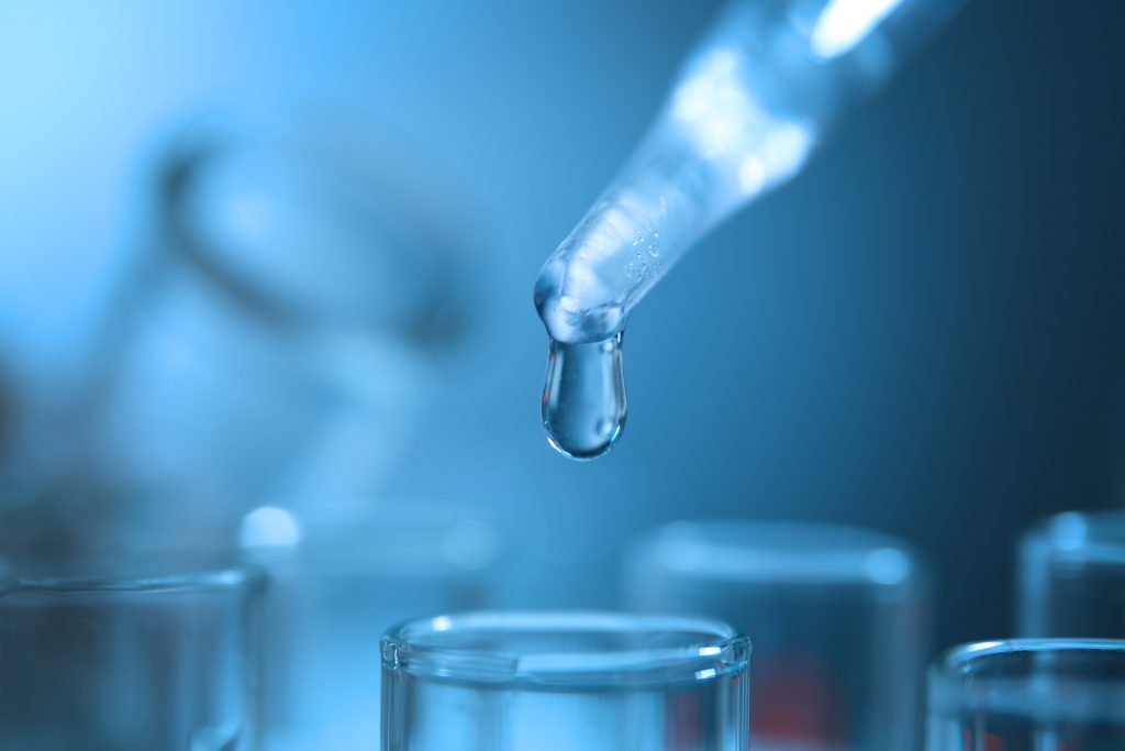Pipette releasing a drop of water over glass laboratory beakers