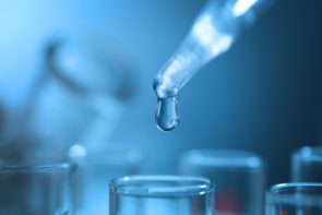 Pipette releasing a drop of water over glass laboratory beakers